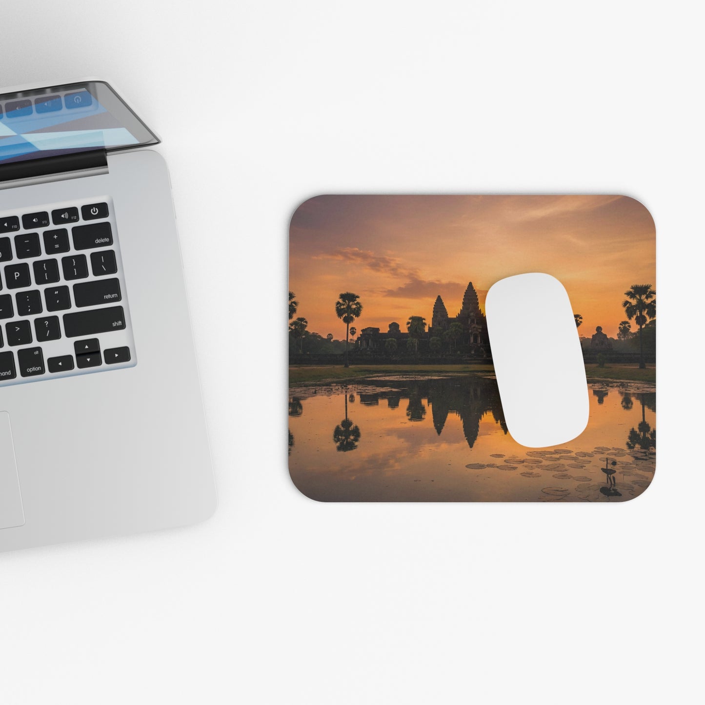 Mouse pad with sunset design next to a laptop on a white surface