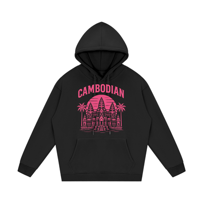 The central artwork uses a bright pink color scheme and includes the following features:

Typography: The word "CAMBODIAN" is printed in a bold, capitalized, sans-serif font that arches over the central image.

Architecture: A detailed illustration of Angkor Wat serves as the centerpiece.

Background: A large, solid circular sun with horizontal line cutouts sits behind the temple, creating a "retro-sunset" or "synthwave" aesthetic.

Nature Details: Two palm trees flank the temple, and horizontal lines at th
