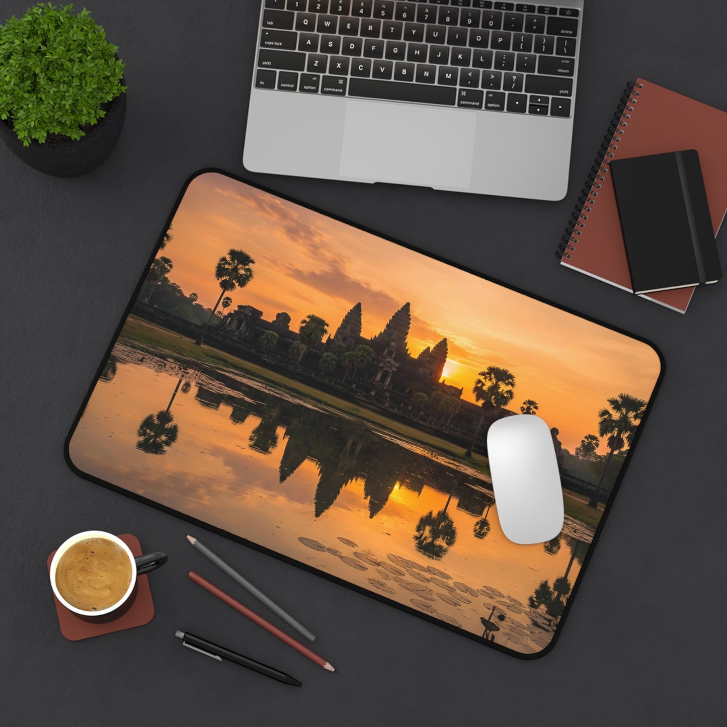 Desk setup with a mouse pad featuring a sunset over water design, laptop, notebook, and coffee cup.