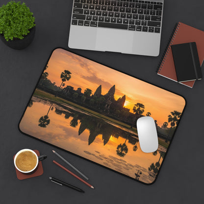Desk setup with a mouse pad featuring a sunset over water design, laptop, notebook, and coffee cup.