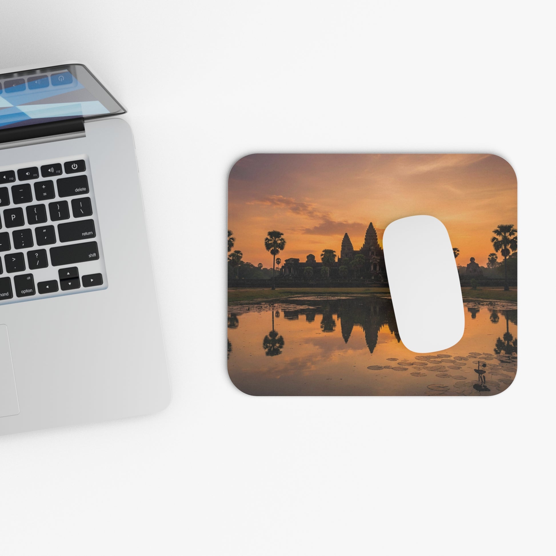 Mouse pad with sunset design next to a laptop on a white surface