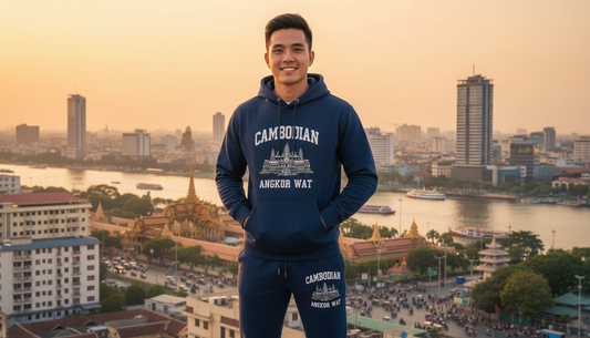 Person wearing a blue hoodie with 'Cambodian' text, standing in front of a cityscape with a river and skyline.