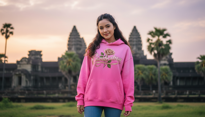 Woman wearing a pink hoodie with text and a rose design, standing in front of Angkor Wat.
