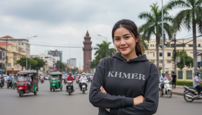 Woman wearing a hoodie with 'KHMER' text on a street with tuk-tuks and buildings in the background