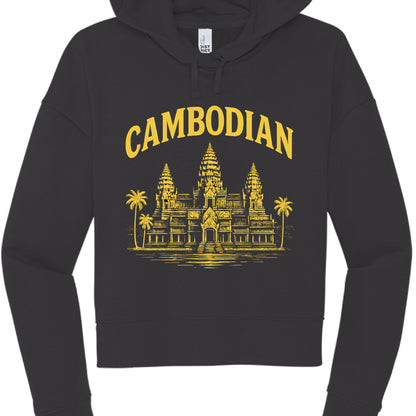 This image showcases a black cropped hoodie with a graphic design centered on the chest, similar in style to the previous version but with a different color scheme.

Design Elements
Text: The word "CAMBODIAN" is printed in a bold, arched, serif font across the top.

Graphic: Below the text is a detailed illustration of Angkor Wat, featuring its characteristic three towers and surrounding palm trees.

Colorway: This version uses a bright yellow (gold) ink for the text and illustration, creating a sharp contr