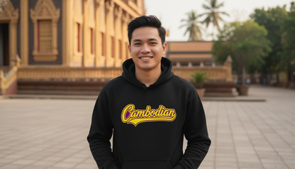 Person wearing a black hoodie with 'Cambodian' text in yellow, standing in front of an architectural structure.