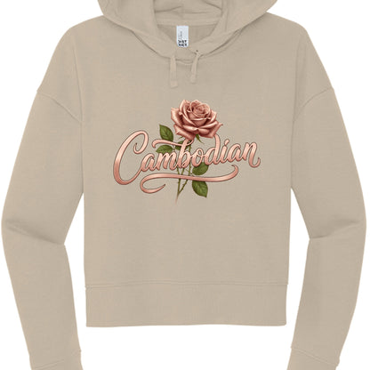 This image features a tan or beige cropped hoodie with a custom graphic design centered on the chest. The overall aesthetic is soft, feminine, and elegant.

Design Details
Typography: The word "Cambodian" is written in a stylized, rose-gold cursive font. The lettering has a metallic, 3D sheen with soft highlights and shadows, giving it a ribbon-like appearance.

Floral Element: A realistic, dusty rose (matching the color of the text) is positioned just above the "m" and "b" in the text. It includes green le