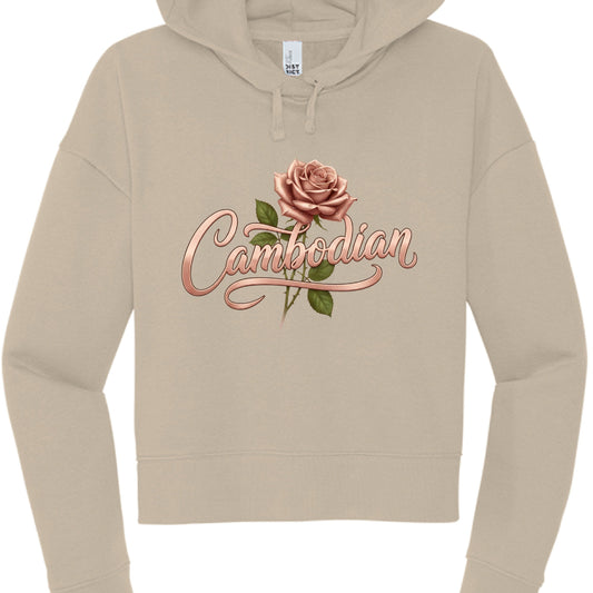 This image features a tan or beige cropped hoodie with a custom graphic design centered on the chest. The overall aesthetic is soft, feminine, and elegant.

Design Details
Typography: The word "Cambodian" is written in a stylized, rose-gold cursive font. The lettering has a metallic, 3D sheen with soft highlights and shadows, giving it a ribbon-like appearance.

Floral Element: A realistic, dusty rose (matching the color of the text) is positioned just above the "m" and "b" in the text. It includes green le