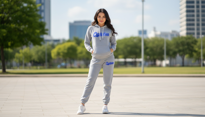 Person wearing a gray hoodie and pants with a brand logo, standing outdoors in an urban setting.