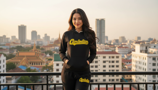 Woman wearing a black hoodie with 'Cambodian' text, standing on a rooftop with a cityscape in the background.