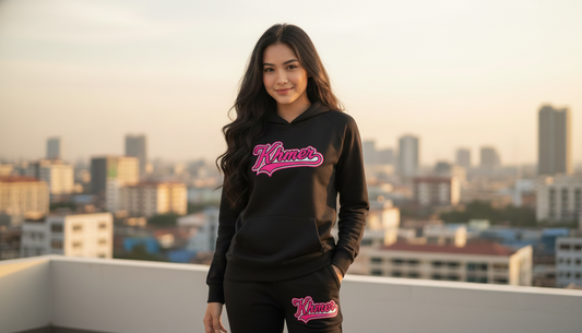 Woman wearing a black hoodie with pink text, standing on a rooftop with a cityscape in the background.