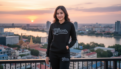 Woman wearing a black hoodie with 'Zumer' branding, standing against a cityscape with a sunset.