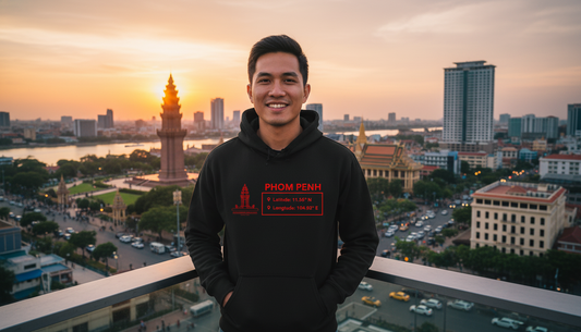 Person wearing a black hoodie with red text standing in front of a cityscape at sunset.