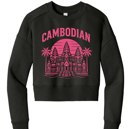 This image features a black, long-sleeved cropped sweatshirt with a vibrant graphic design centered on the chest.

Design Details
The graphic is rendered in a bright pink (magenta) ink and follows a retro, synthwave-inspired aesthetic:

Typography: The word "CAMBODIAN" is arched across the top in a bold, sans-serif block font.

Illustration: The centerpiece is a detailed, stylized illustration of Angkor Wat, the famous temple complex in Cambodia.

Background Elements: * A large, circular "sunset" with horiz