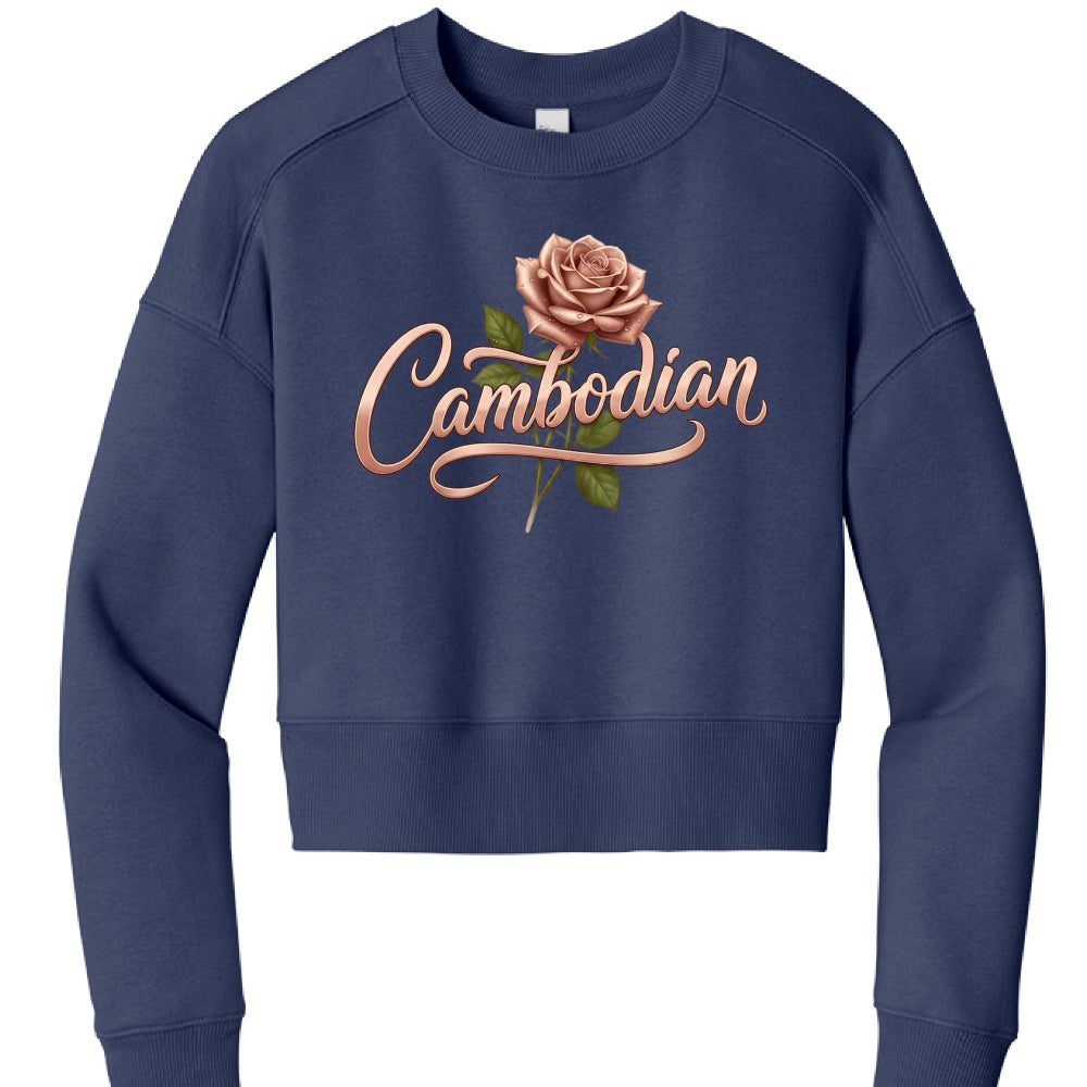 This image features a navy blue, cropped sweatshirt displayed against a plain white background. The garment has a casual, modern fit with a round crew neck and ribbed cuffs and hem.

The central focus of the sweatshirt is a graphic design that includes:

Floral Illustration: A realistic, rose-gold or dusty pink rose in full bloom, complete with green leaves and a stem.

Typography: The word "Cambodian" is written across the rose in a stylized, rose-gold metallic script. The font features elegant flourishes,