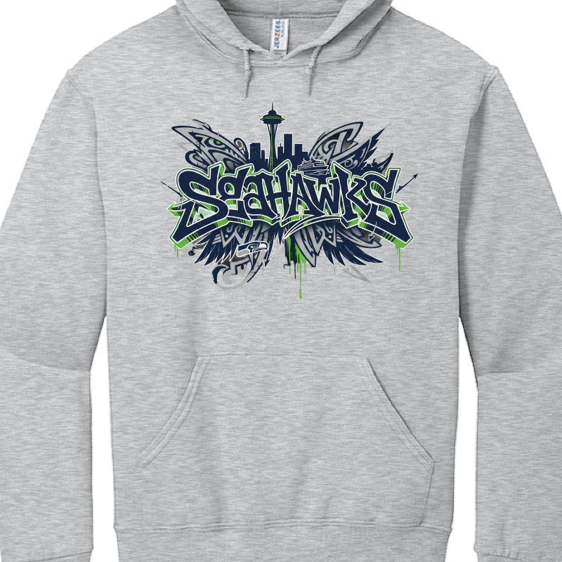 Heather Grey Hoodie (Image 2)
This garment features a lighter grey fabric and a design that emphasizes the Seattle waterfront:

Typography: The "SEAHAWKS" text uses a similar navy and action green graffiti font, accented by green paint drips at the bottom.

Background Skyline: The silhouette of the Seattle skyline is more prominent here, featuring the Space Needle and a Washington State Ferry.

Wing Motifs: Abstract, tribal-influenced wing shapes spread out from behind the text, creating a symmetrical, "win
