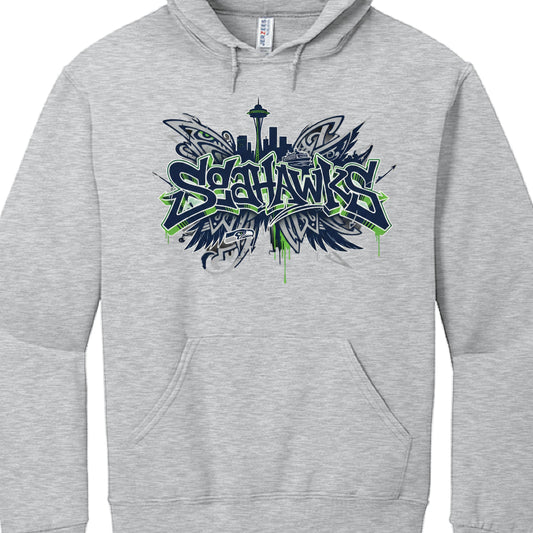 Heather Grey Hoodie (Image 2)
This garment features a lighter grey fabric and a design that emphasizes the Seattle waterfront:

Typography: The "SEAHAWKS" text uses a similar navy and action green graffiti font, accented by green paint drips at the bottom.

Background Skyline: The silhouette of the Seattle skyline is more prominent here, featuring the Space Needle and a Washington State Ferry.

Wing Motifs: Abstract, tribal-influenced wing shapes spread out from behind the text, creating a symmetrical, "win