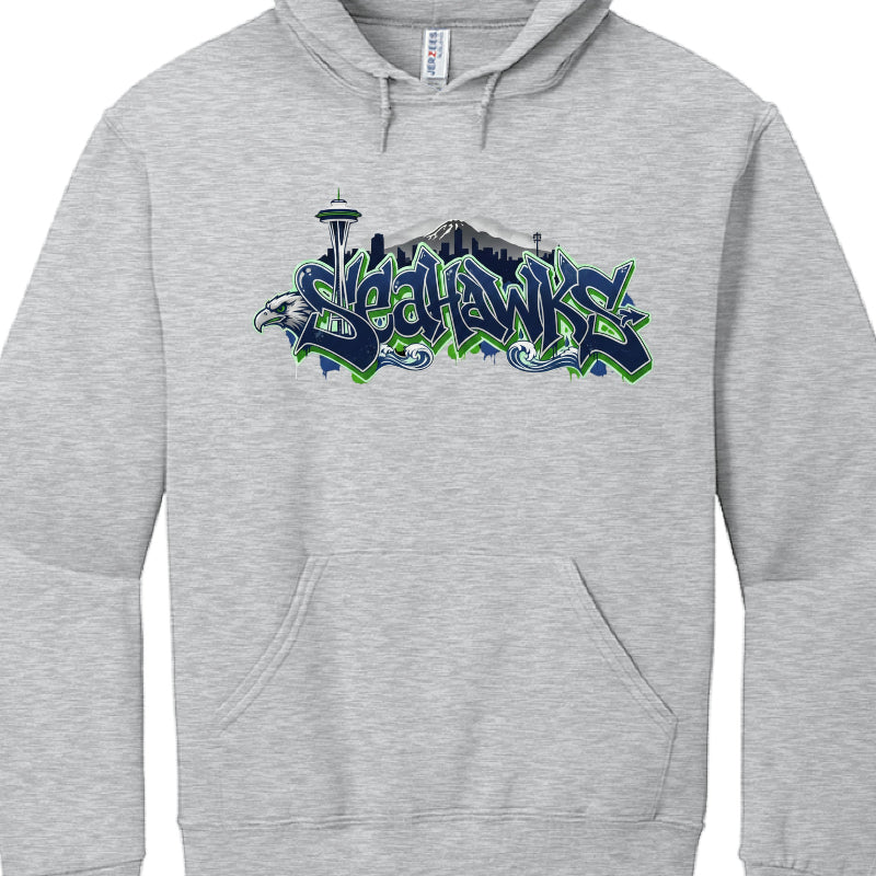 These hoodies celebrate the Seattle Seahawks with stylized graphics incorporating the team's colors and iconic Seattle landmarks.

Northwest Coast Style (image_a4521c.jpg): A black hoodie featuring a central osprey (seahawk) rendered in an indigenous art style. The Space Needle rises behind the bird, and the word "SEAHAWKS" is printed in a bold, green and blue 3D-effect font.

Graffiti Skyline Style (image_a455be.jpg): A heather grey hoodie featuring the word "SEAHAWKS" in a navy and neon green graffiti-sty