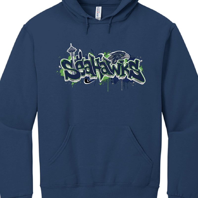 These hoodies celebrate the Seattle Seahawks with designs incorporating team colors and iconic landmarks like the Space Needle and Mount Rainier.

Northwest Coast Style (image_a4521c.jpg): A black hoodie featuring an osprey (seahawk) rendered in a traditional indigenous art style. The Space Needle is centered behind the bird, and the word "SEAHAWKS" is printed in a bold, 3D-effect font.

Graffiti Skyline Style: These designs feature a stylized, dripping graffiti font for the word "SEAHAWKS" set against vari