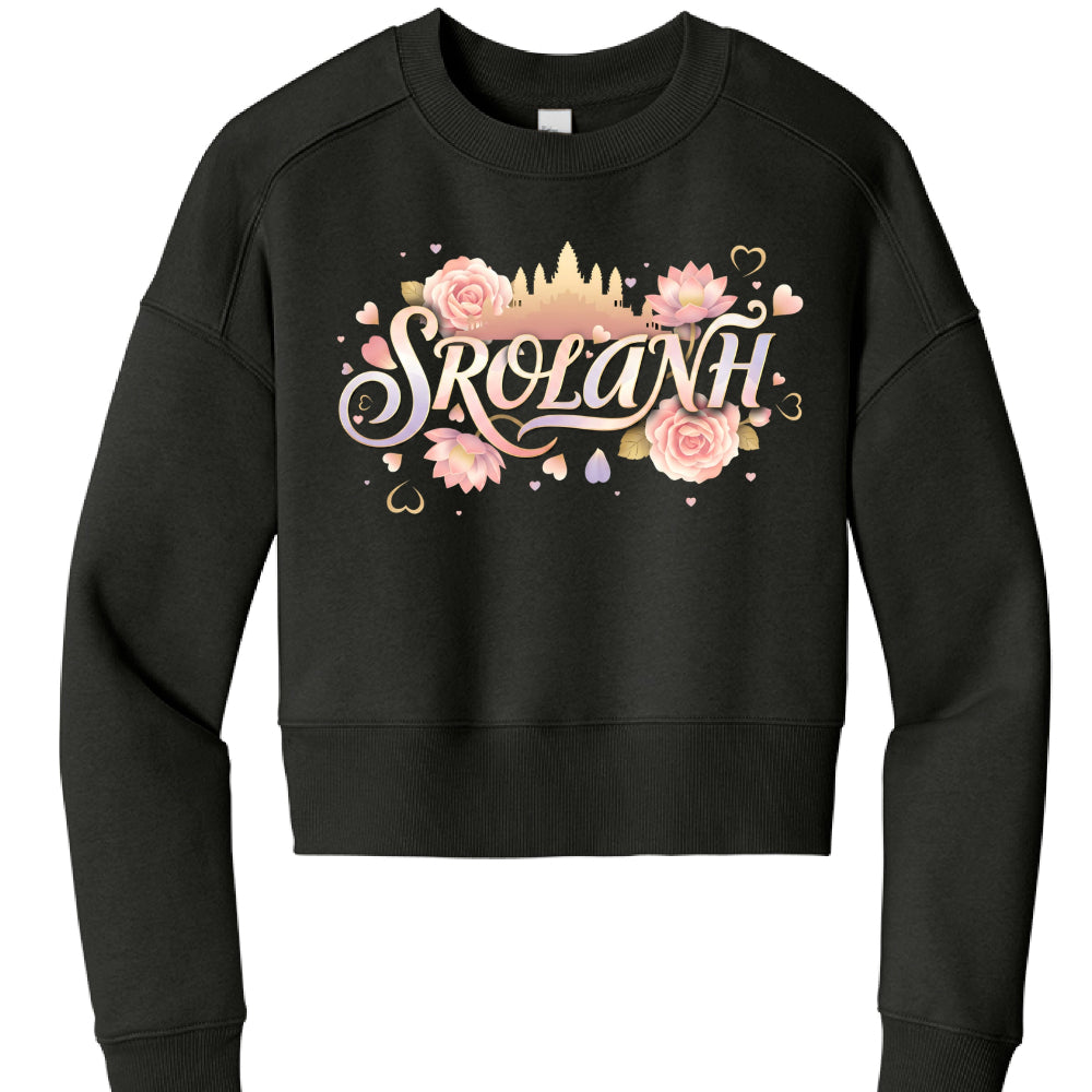 The image features a black, long-sleeved cropped sweatshirt with a vibrant, illustrative graphic centered on the chest. The design blends cultural symbols with a soft, romantic aesthetic.

Graphic Details
The central focus is the word "SROLANH" (a Khmer word for "love") written in an elegant, stylized script with a pastel gradient of pink, purple, and cream.

Background Silhouette: Behind the text is a golden-tan silhouette of Angkor Wat, the famous Cambodian temple complex.

Floral Accents: The text is sur