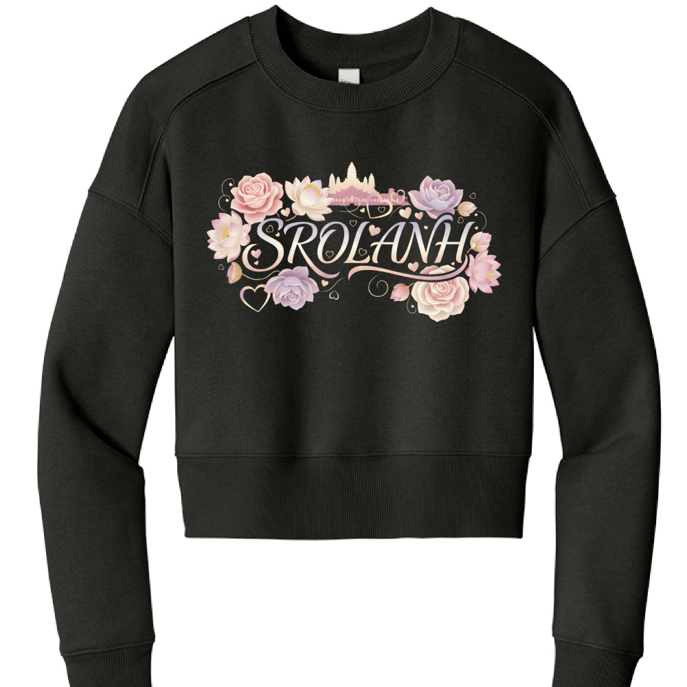 This image shows a black cropped sweatshirt featuring a decorative graphic design on the chest.

Garment Features
Style: A long-sleeved, crewneck sweatshirt with a cropped silhouette that hits above the waist.

Details: It includes dropped shoulders and a wide ribbed waistband and cuffs.

Color: The fabric is a solid, deep black.

Graphic Design
Text: The center of the design features the word "SROLANH" in an elegant, cursive serif font with a light peach-to-white gradient.

Floral Elements: The text is sur