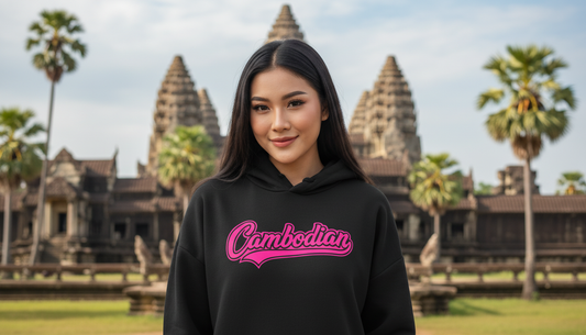 Person wearing a black hoodie with 'Cambodian' text in pink, standing in front of Angkor Wat.