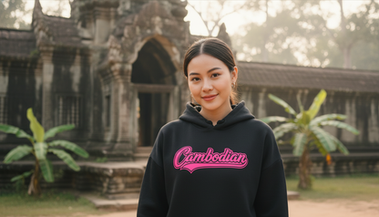 Person wearing a black hoodie with 'Cambodian' text in pink, standing in front of temple ruins.