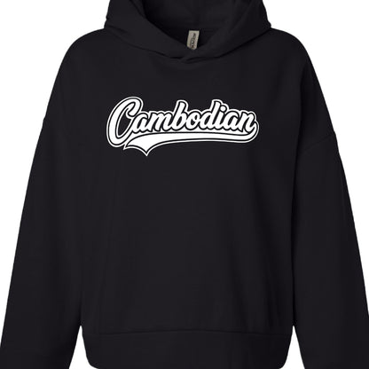 Color: Solid black.

Garment Style: It appears to be a heavy-weight or oversized hoodie, featuring dropped shoulders and a front kangaroo pocket. A small white manufacturer's tag is visible inside the collar.

Graphic Design:

Text: The word "Cambodian" is printed in the center.

Typography: The font is a white, retro-style cursive script with a thick black outline.

Accents: A stylized "swoosh" or underline extends from the bottom of the letter "n," giving it a classic athletic or "varsity" aesthetic.